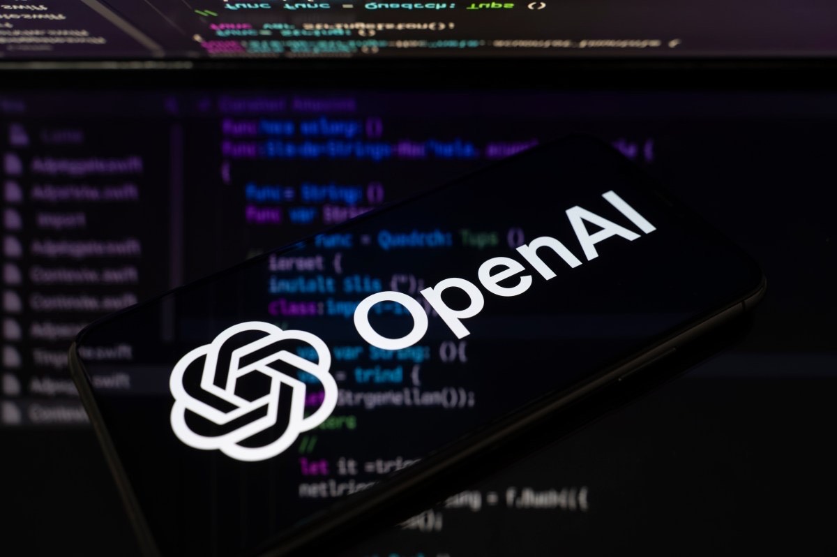 手机屏幕上的 OpenAI 标志，背景是模糊的代码编辑器
